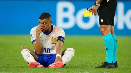 Kylian Mbappé de Francia sentado en el campo, con la mano sobre la nariz ensangrentada, mientras el árbitro sostiene la tarjeta amarilla, durante un partido del Grupo D contra Austria (AP)