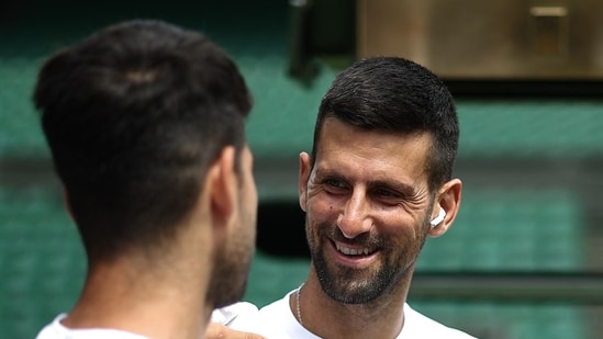 El serbio Novak Djokovic sonríe al español Carlos Alcaraz durante una sesión de calentamiento en la cancha central del All England Lawn Tennis Club, en el oeste de Londres, el 27 de junio de 2024, la semana antes del Campeonato de Wimbledon (AFP)