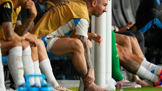 El argentino Lionel Messi se toca el tobillo sentado en el banquillo durante la final de la Copa América contra Colombia en Miami Gardens (AP)