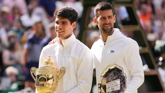 Carlos Alcaraz de España sostiene su trofeo junto a Novak Djokovic de Serbia después de ganar la final individual masculina en Wimbledon (AP)