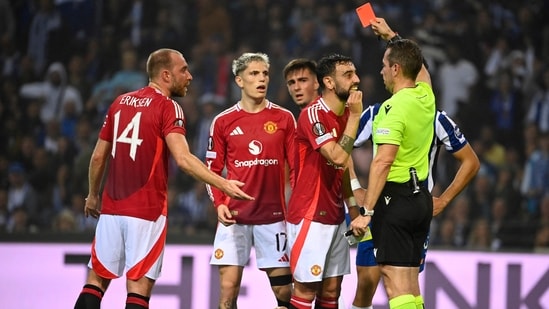 El mediocampista portugués del Manchester United #08 Bruno Fernandes (2R) protesta ante el árbitro alemán Tobias Stieler mientras le presentan una tarjeta roja por cometer una falta contra el defensa argentino del FC Porto (AFP)