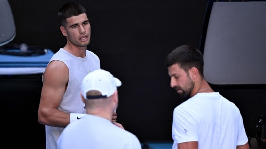 El español Carlos Alcaraz (i) conversa con el serbio Novak Djokovic (d) durante una sesión de entrenamiento antes del torneo de tenis Abierto de Australia en Melbourne el 7 de enero de 2025. (AFP)